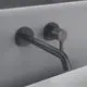 Wand-Waschtischarmatur in mattem Schwarz von Ideal Standard, mit runden Rosetten und einer ausgezogenen Armatur. Montiert an einer grauen Wand.